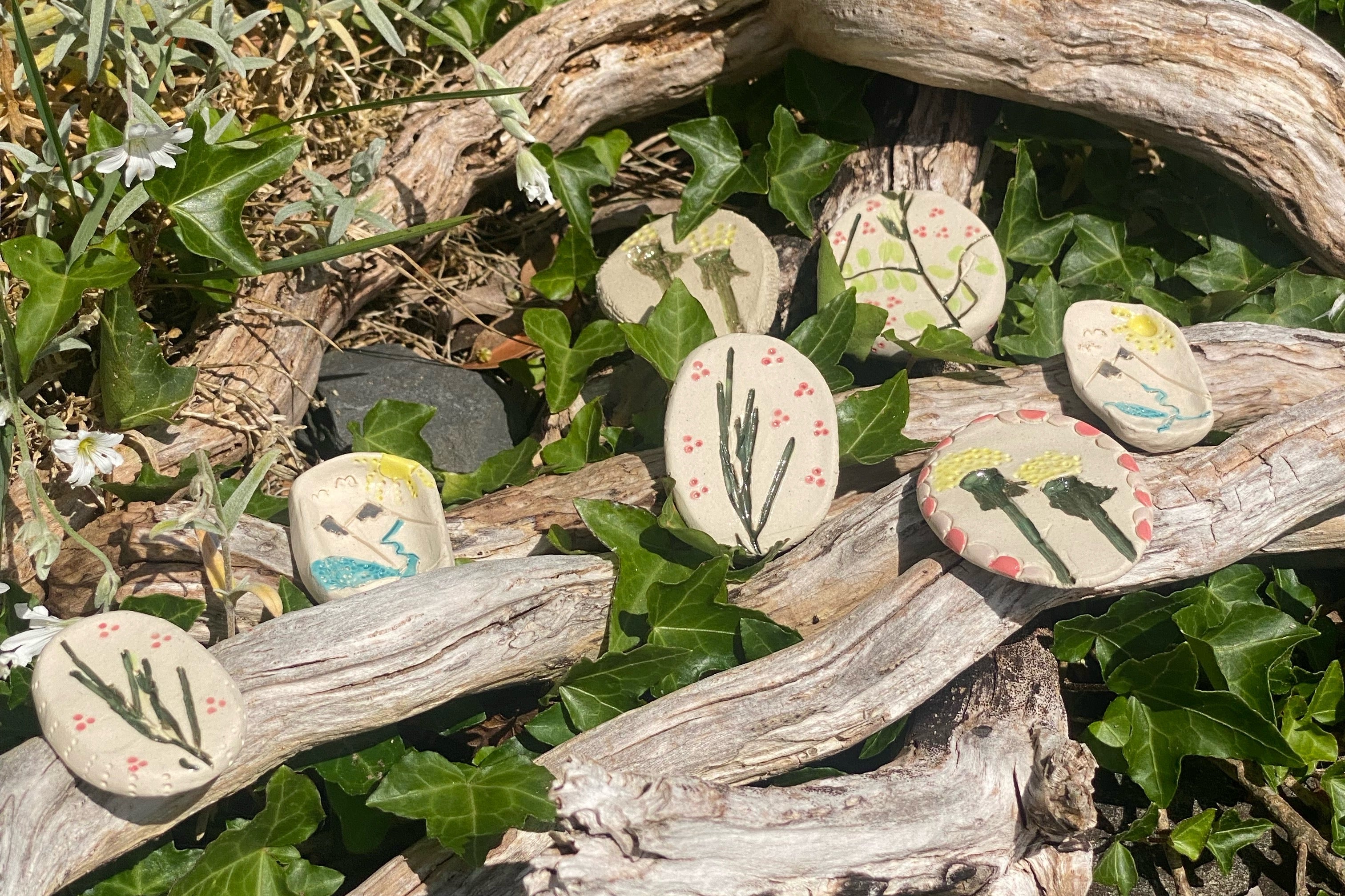 Decorative ceramic fidget stones with plant designs on a bed of green leaves and twigs